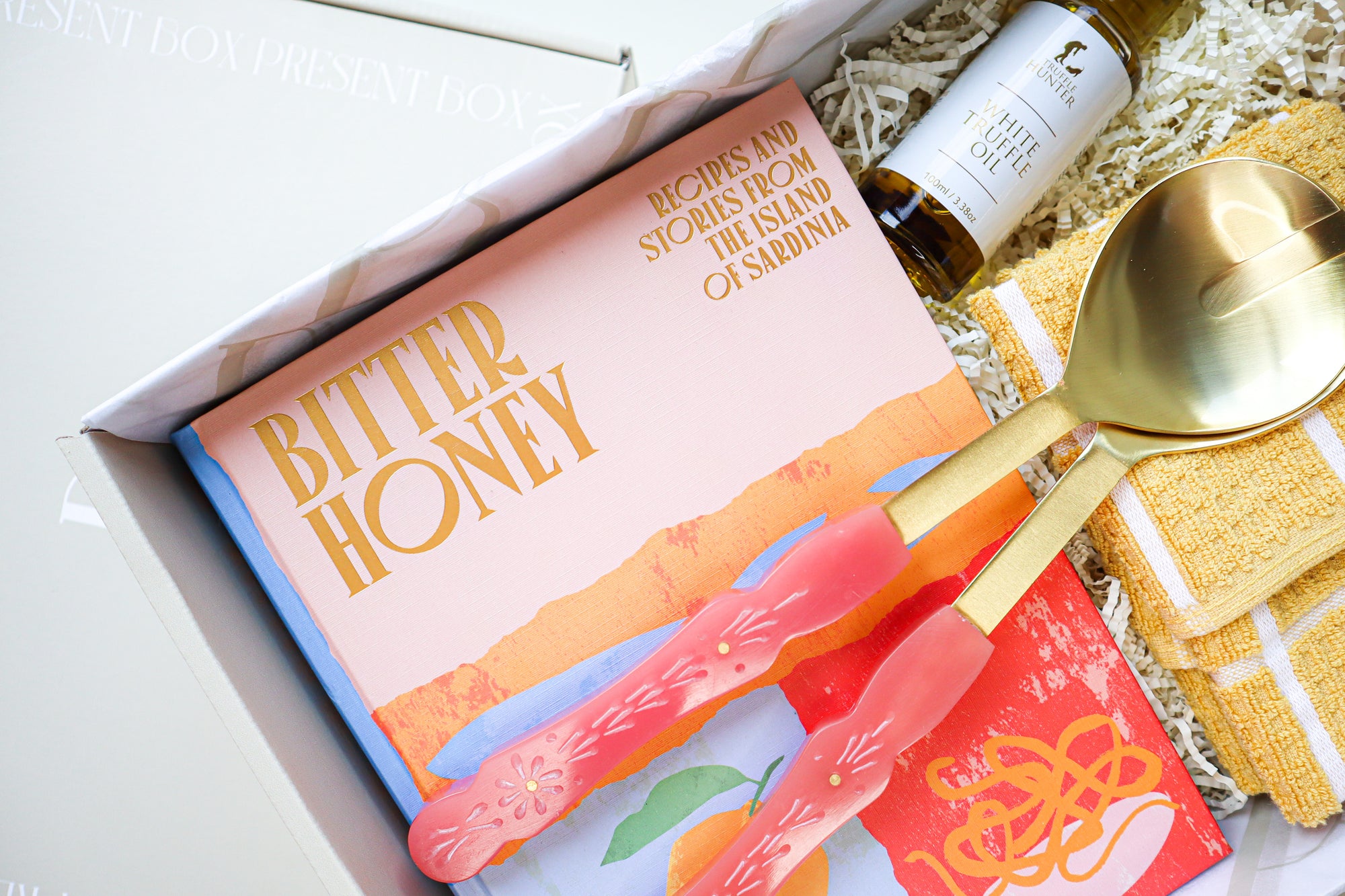A beautiful, brightly coloured, hard cover cook book titled Bitter Honey with 2 pink and gold salad servers and a small bottle of White Truffle Oil in a gift box