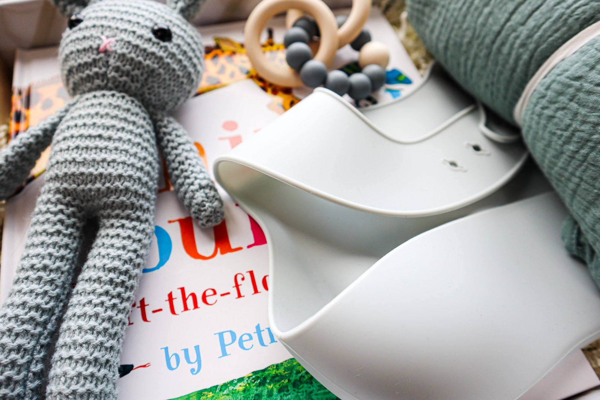 A cute blue crocheted bunny lying on it's back, a folded light blue silicone baby bib, lying on a children's book titled Animal Counting